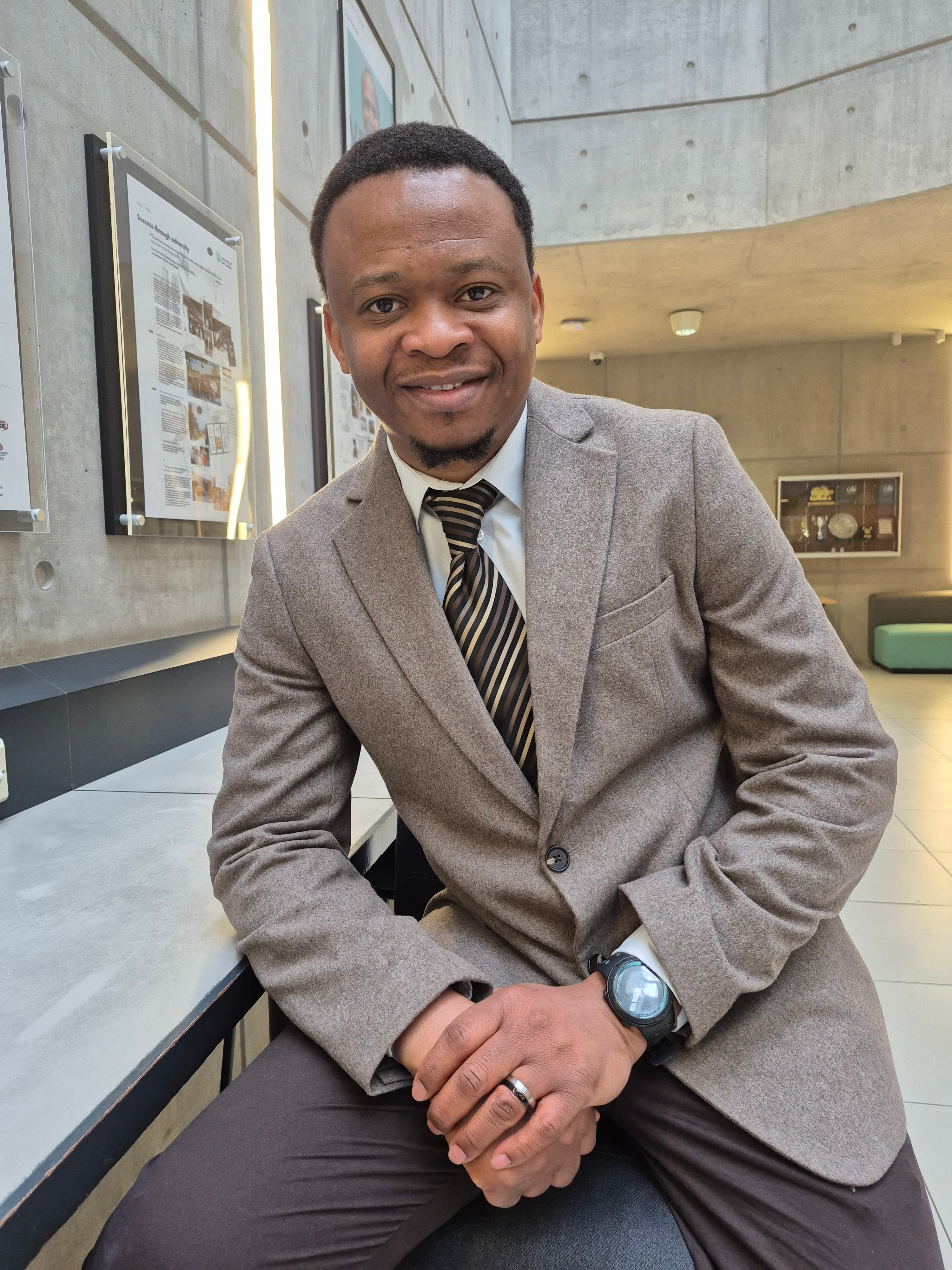 Smiling Black man in a brown textured blazer and striped tie in a modern building.