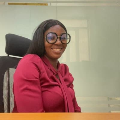 Smiling woman wearing large geometric glasses and a magenta blouse in an office setting.